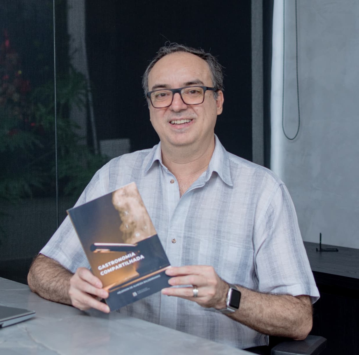 Helerson de Almeida Balderramas segurando a edição impressa de Gastronomia Compartilhada, em luz natural